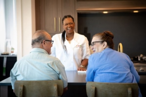 Personal chef laughing with an elderly couple in their kitchen.