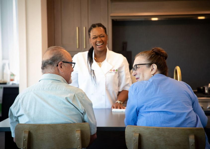 Personal chef laughing with an elderly couple in their kitchen.
