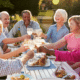 Seniors smile and laugh while drinking and eating at an outdoor dinner party