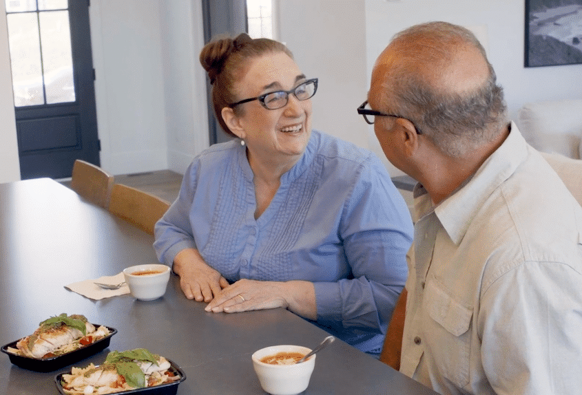 Elderly couple smiling while enjoying a fresh made meal from Chefs For Seniors at the kitchen island in their own home