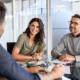 A couple sits smiling at a table with calculator and notebook across from a financial advisor