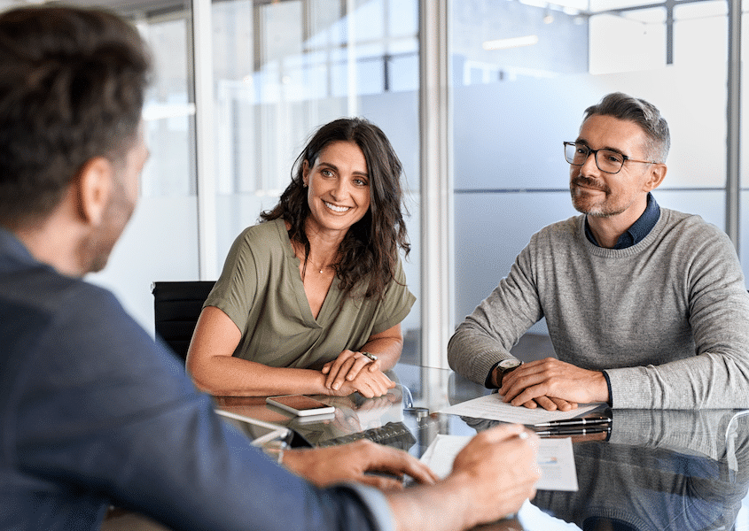 A couple sits smiling at a table with calculator and notebook across from a financial advisor