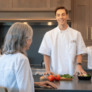 Chefs For Seniors personal chef prepares a meal at the kitchen island while a happy client watches